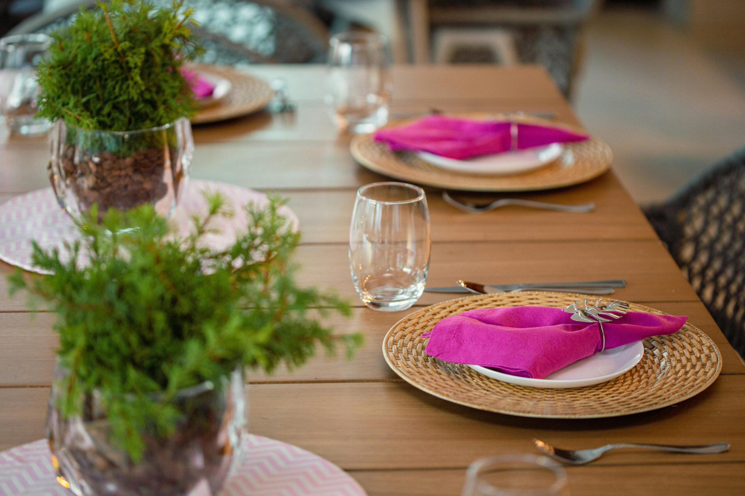 A beautifully arranged dining table with pink napkins and plant centerpieces, perfect for a stylish event.